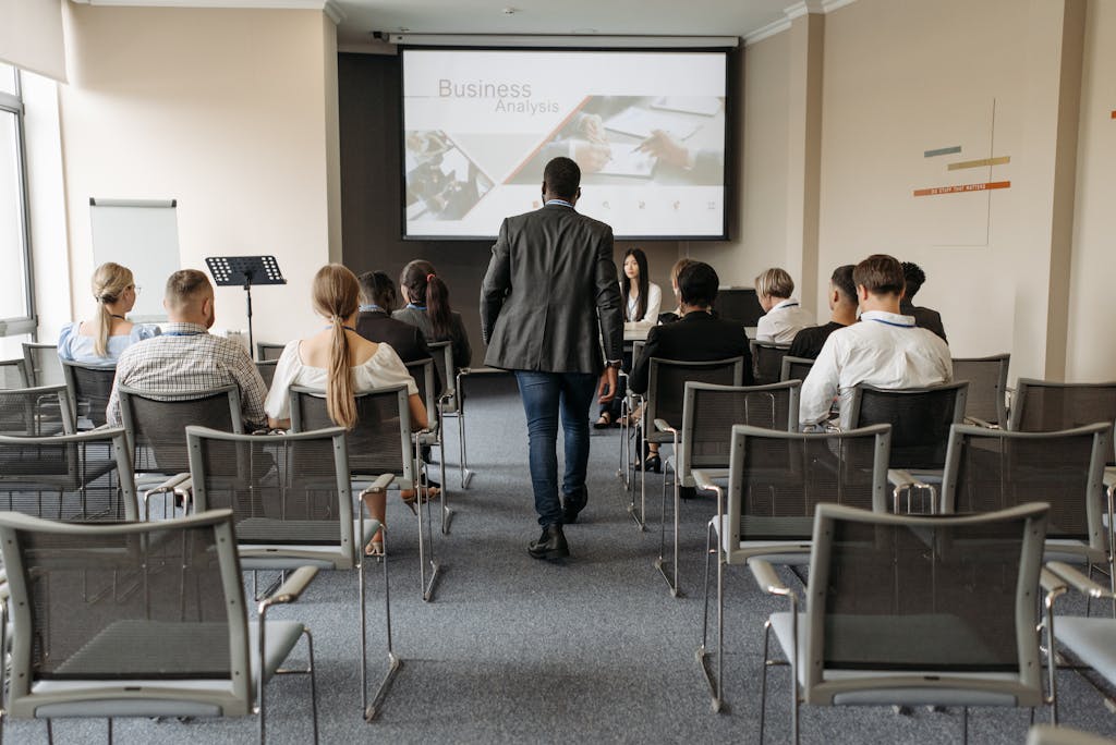 A Man Walking on Aisle Between Chairs with People Sitting